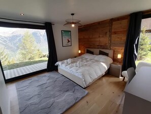 A bedroom with a large bed, a nightstand, a lamp, a view of mountains, and a wooden wall. - Chalet, Ground floor, terrace, fireplace or stove, tv, 151m², Montalbert (Aime)