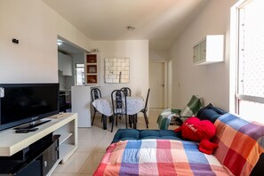A living room with a TV, sofa, and a dining area with chairs and a table. - Apto a 300 m da Praia do Sul com Piscina e Quadra (Ilhéus)