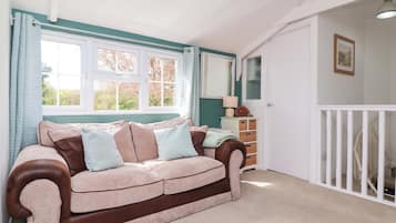 A cozy room with a brown and beige sofa, a window with curtains, a white dresser, and a white railing.