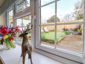 A window with a deer figurine, a vase of flowers, and a view of a backyard with a wooden fence, a bench, and a garden. - The Apple Loft (Exeter)