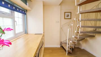 A room with a wooden desk, a window with a view, a staircase, and a framed picture on the wall.