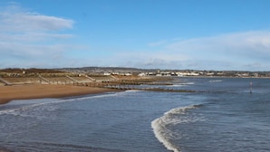 En strand vid kusten med en träbrygga och en sandstrand.
