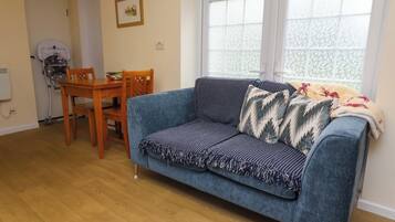 A living room with a blue sofa, wooden dining table, chairs, and a window with patterned curtains.