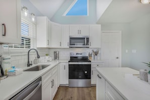 A modern kitchen with white cabinets, stainless steel appliances, and a skylight. - Oceanview | Coastal Haven | Steps to the Beach | 3BR | Fire Pit | 2 10x10 tents & 8 chairs included (Gulf Shores)