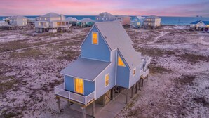 Een huis aan het strand met een balkon, gebouwd op palen en uitzicht op de oceaan.