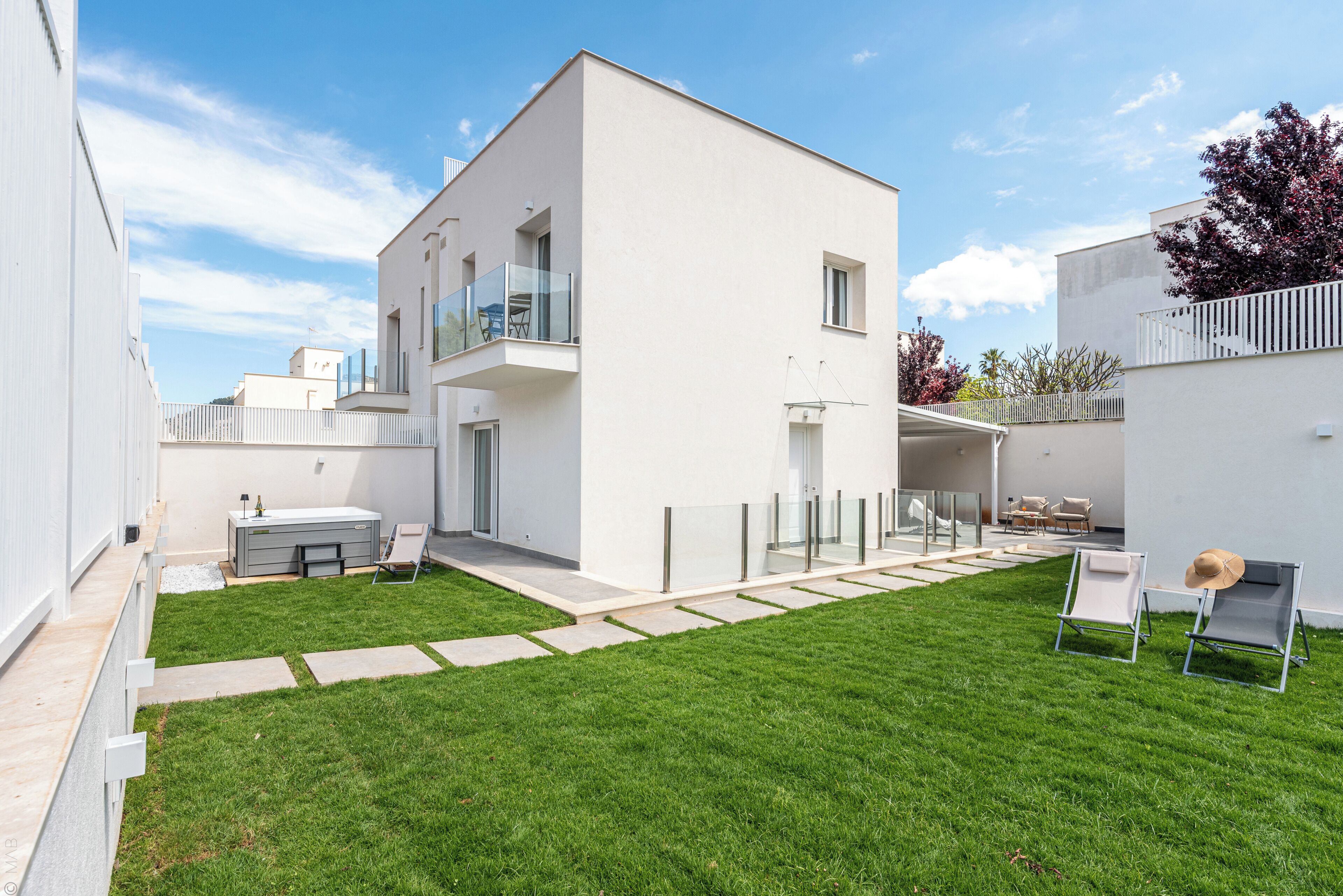 A modern building with a flat roof, a balcony, and a well-maintained lawn.