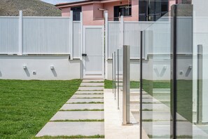 Un vialetto che conduce a un cancello con recinzione bianca, un’area verdeggiante e un edificio dalla facciata rosa.