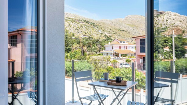 Un balcón con una mesa, sillas y vistas a una colina con edificios.