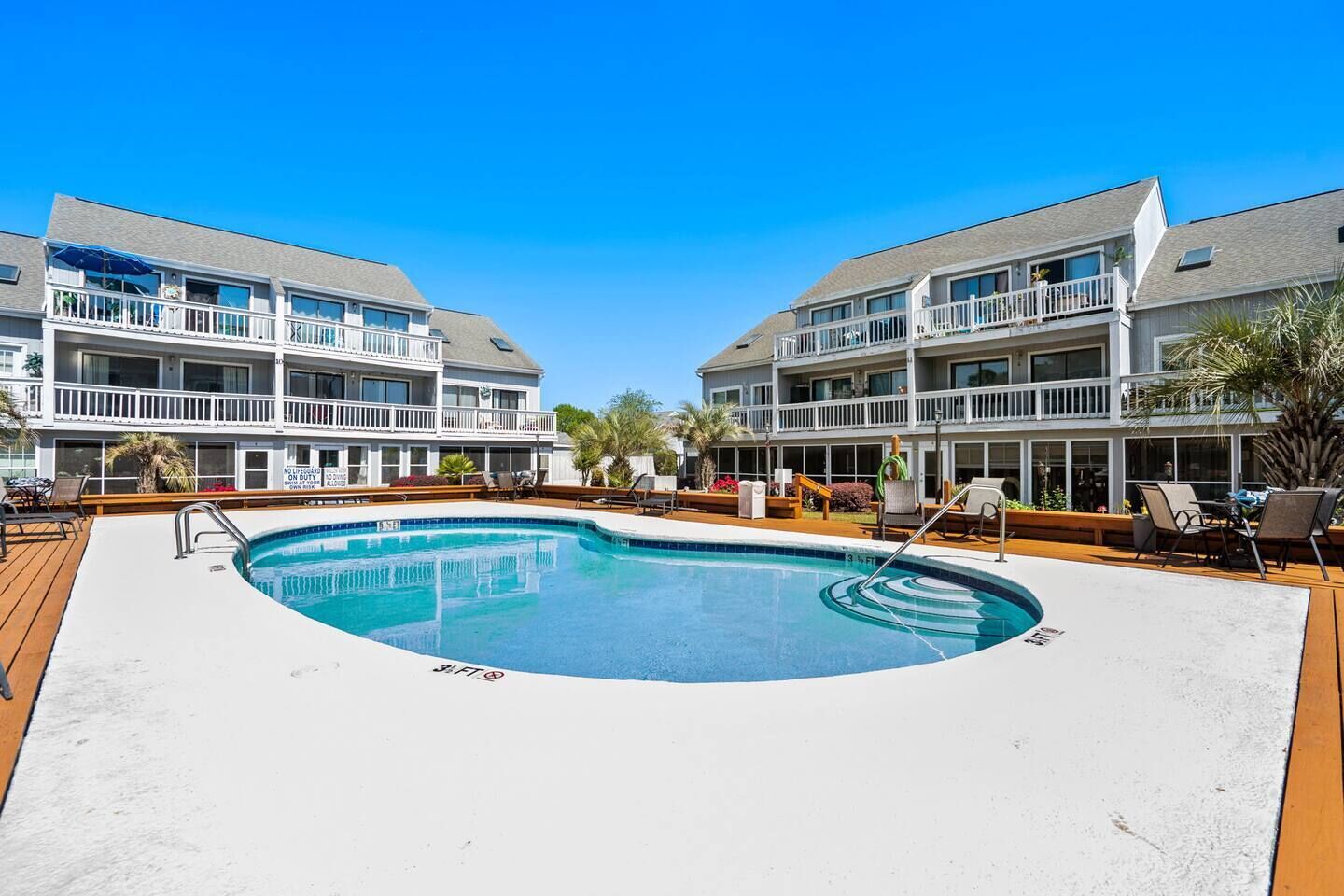 A hotel with a swimming pool, outdoor seating, and a two-story building with balconies.