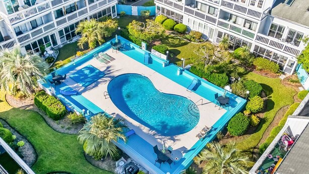 Ein Luftbild eines Hotels mit Swimmingpool, mehreren Balkonen und üppiger Bepflanzung.