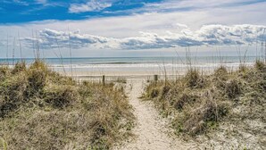Ein Strandweg, der zum Meer führt, mit blauem Himmel.