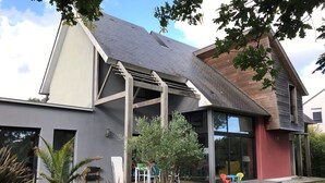 Ett modernt hus med en stor glasdörr, ett trädäck och utomhusmöbler.