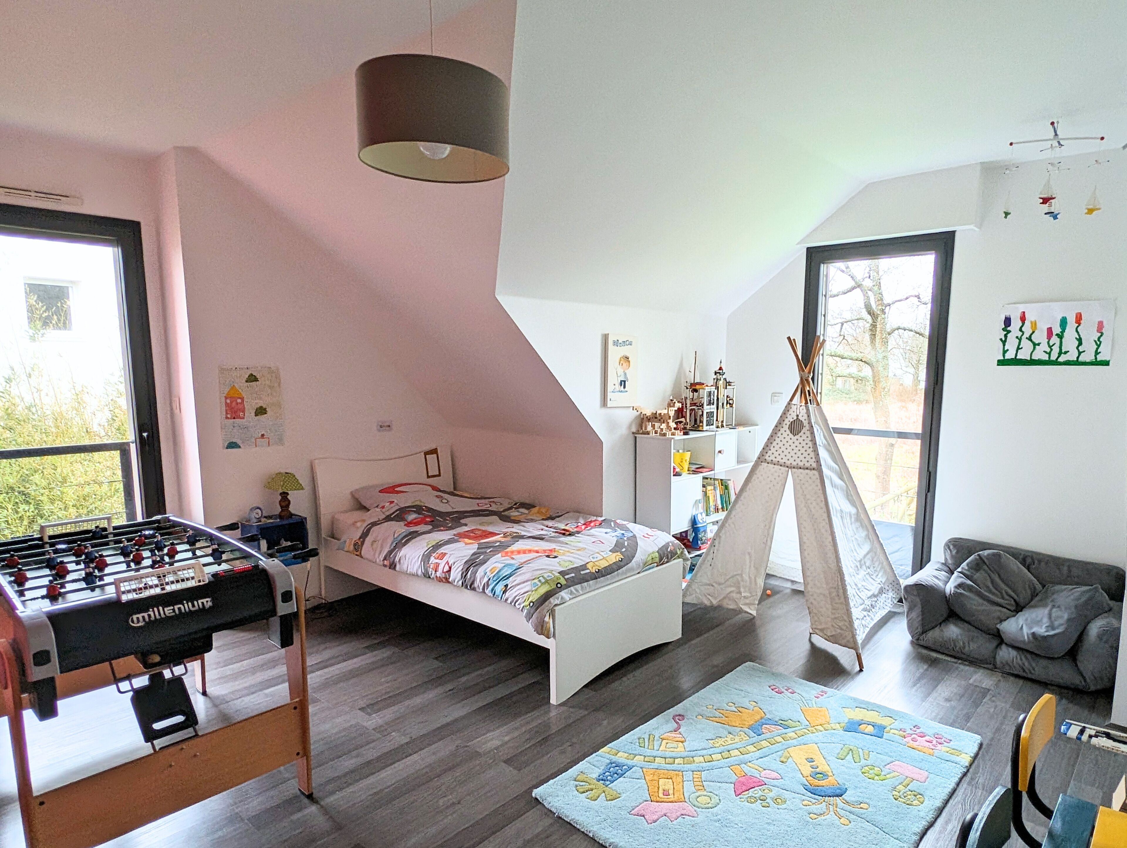 A child's bedroom with a bed, a foosball table, a tent, and a window with a view.