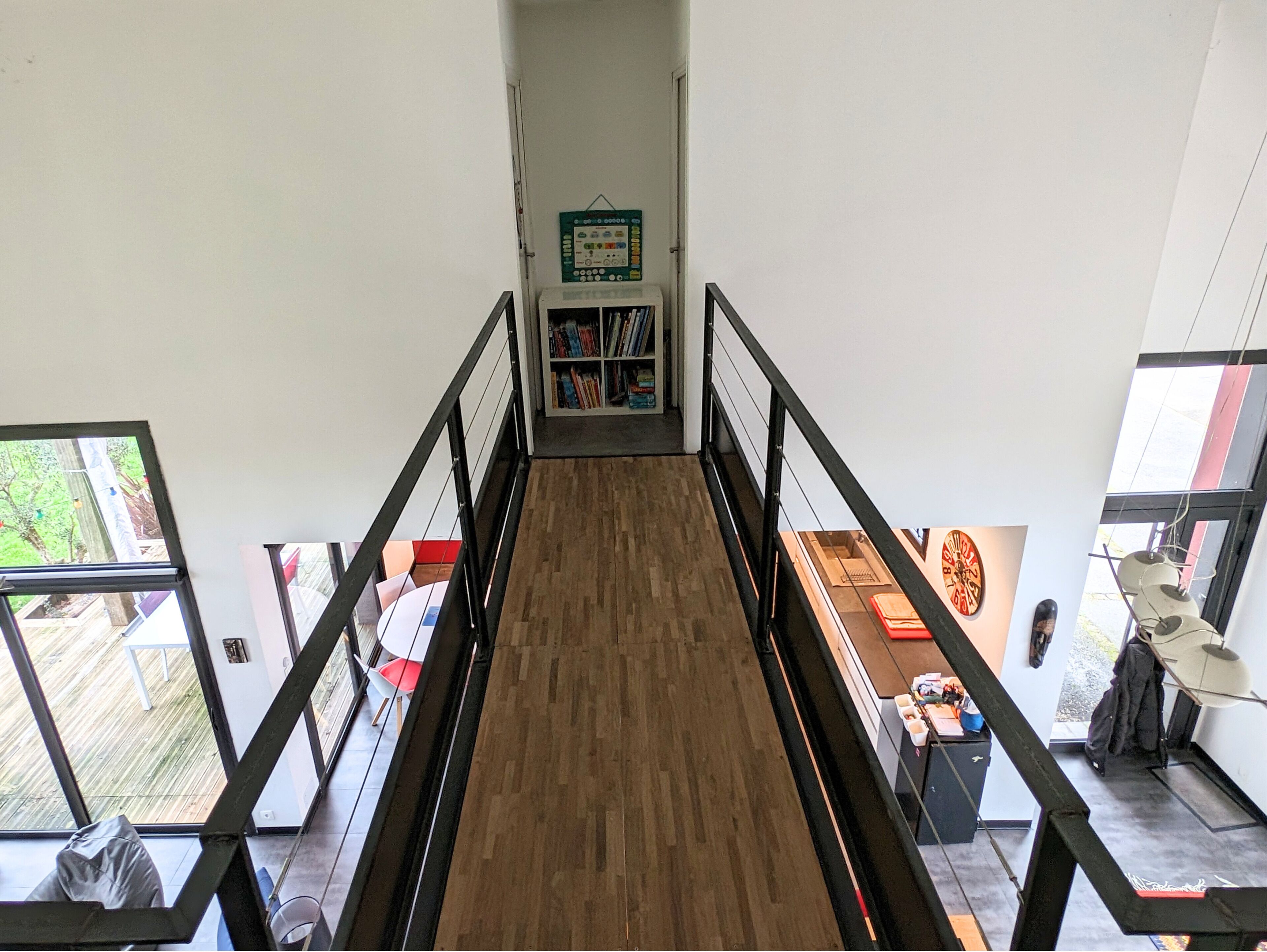 A staircase with a wooden floor and black railings leading to a room with a bookshelf and a door.