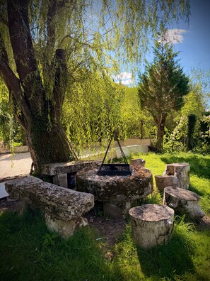 A natural outdoor setting with a tree, a metal grill, and stone seating.