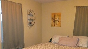 Un dormitorio con cama, mesita de noche, un reloj de pared y ventana con cortinas.