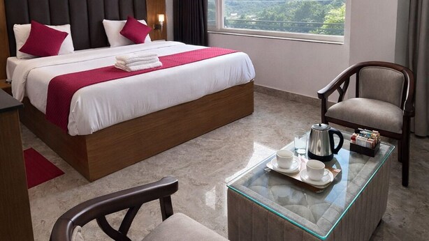 A hotel room with a bed, a chair, a coffee table, a ceiling fan, and a window with a mountain view. - RNR Retreat Serenity By The Ganges (Rishikesh)