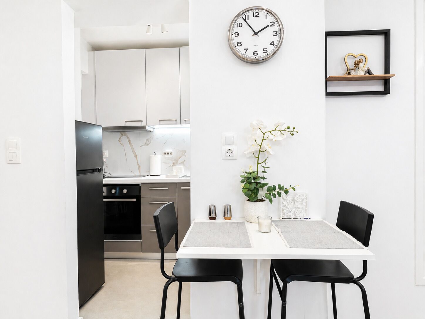 Una cocina moderna con armarios blancos, un refrigerador negro y un salpicadero de mármol.