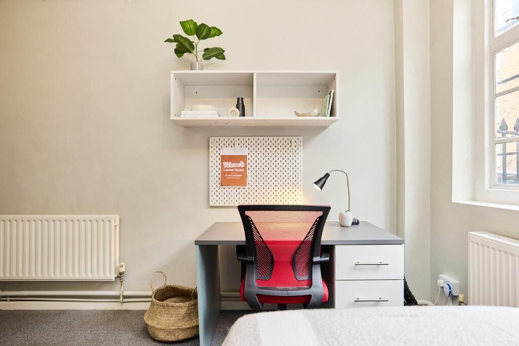 Une pièce comprenant un bureau, une chaise, un radiateur et une fenêtre.