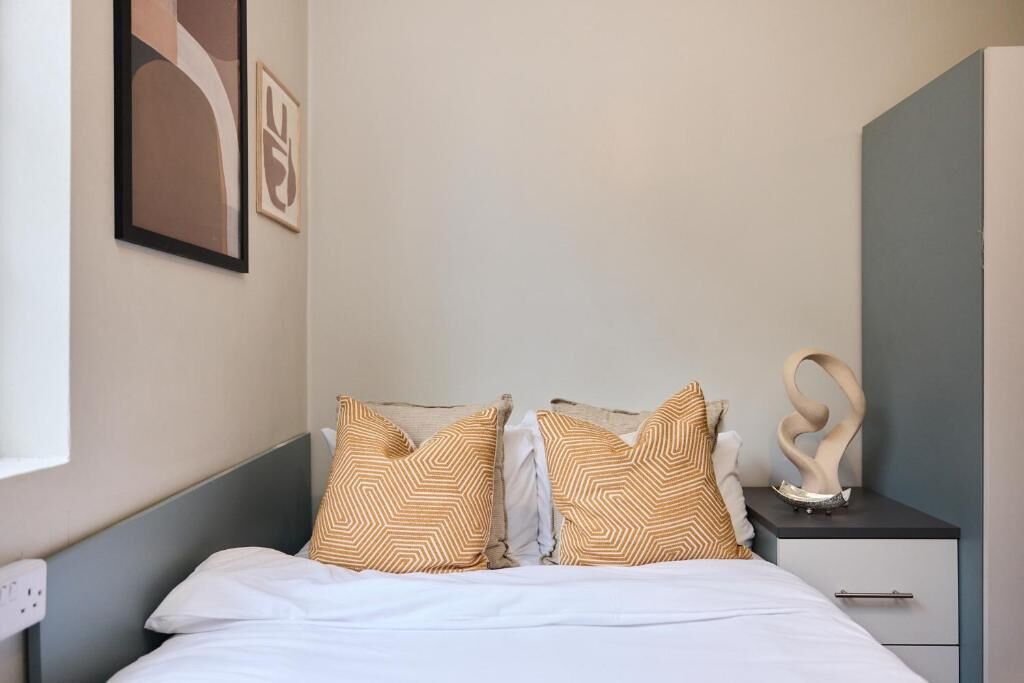A neatly made bed with patterned pillows, a bedside table with a decorative item, and a wall-mounted abstract artwork.