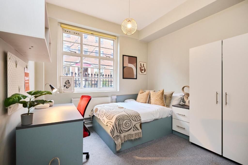 Une chambre à coucher comprenant un lit, un bureau, une chaise, une armoire, une fenêtre et un luminaire suspendu.
