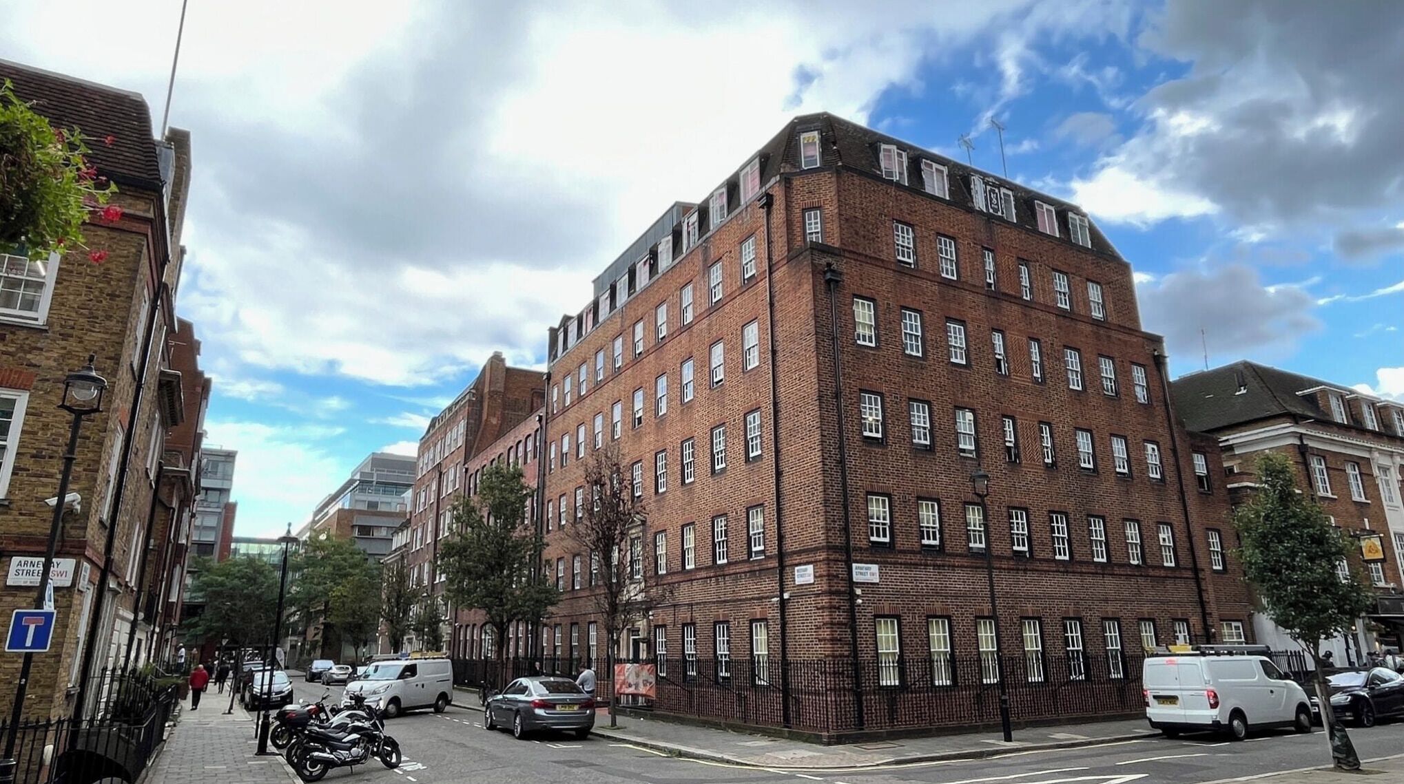 A multi-story brick building with a corner entrance, parked cars, and a clear sky.