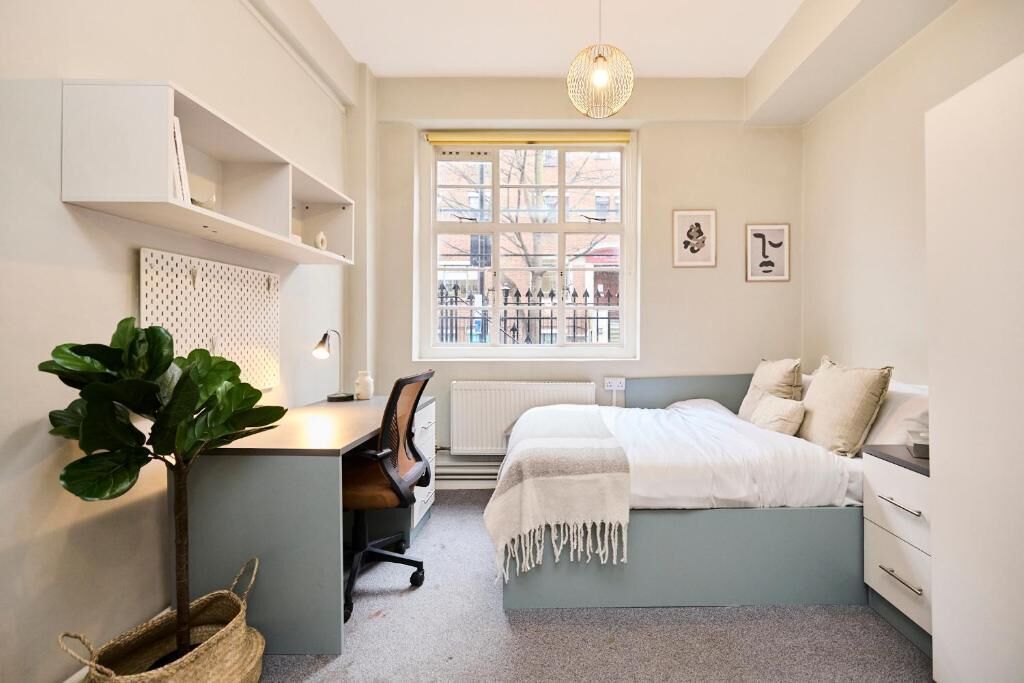A bedroom with a bed, desk, chair, and a large window.