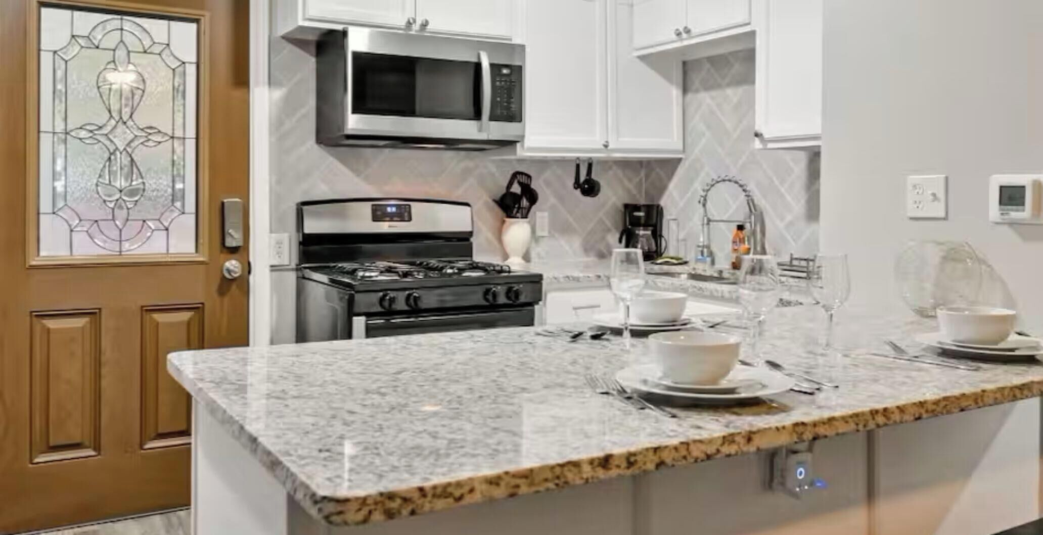 A kitchen with a granite countertop, stainless steel appliances, and a white tiled backsplash.