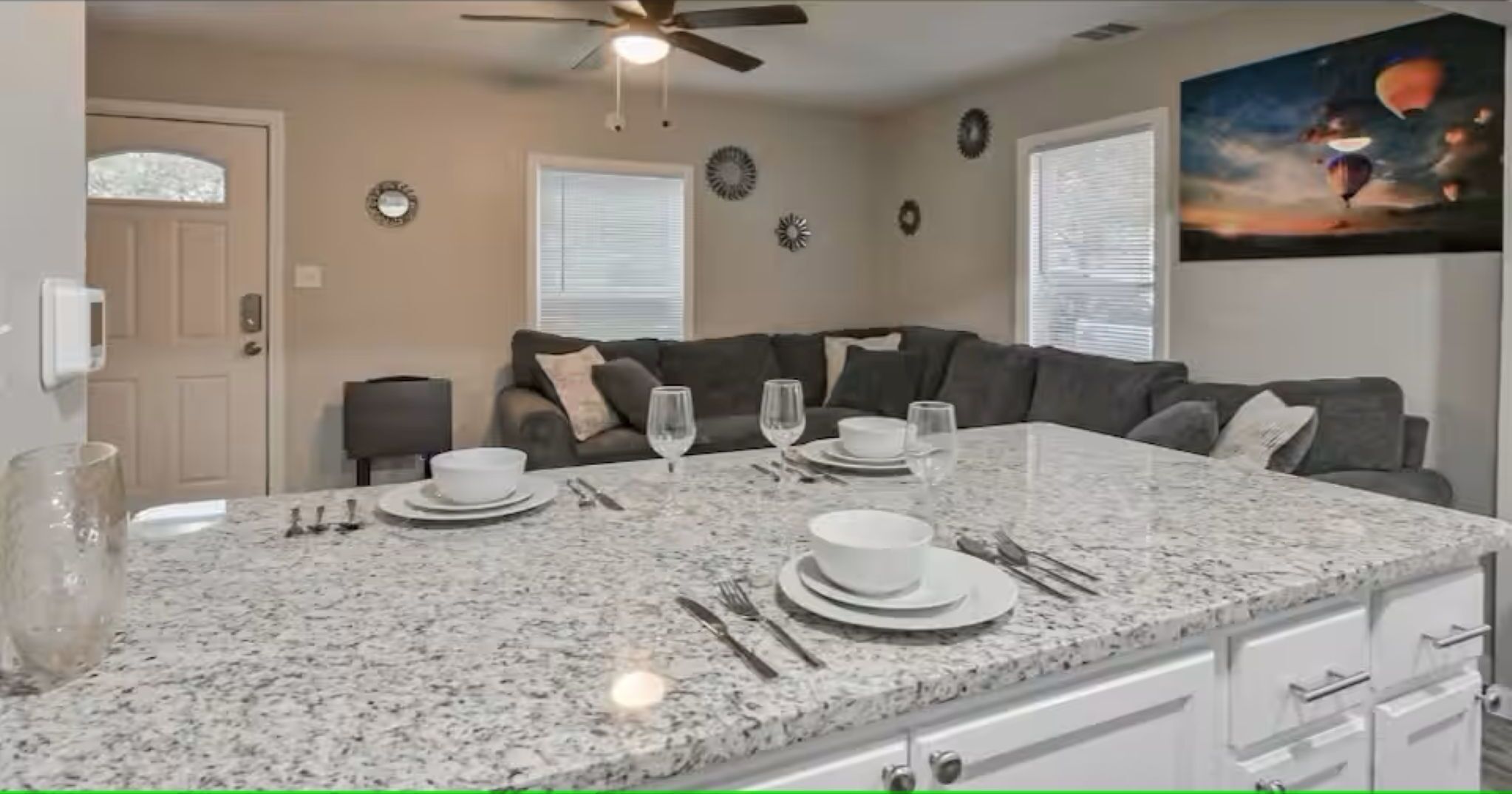 A kitchen with a granite countertop, white cabinets, and a dining area with a table set for two.