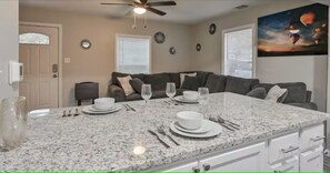 A kitchen with a granite countertop, white cabinets, and a dining area with a table set for two. - Bob Marley Pool Party Bar Hot Tub BBQ & Fire Pit (Arlington)