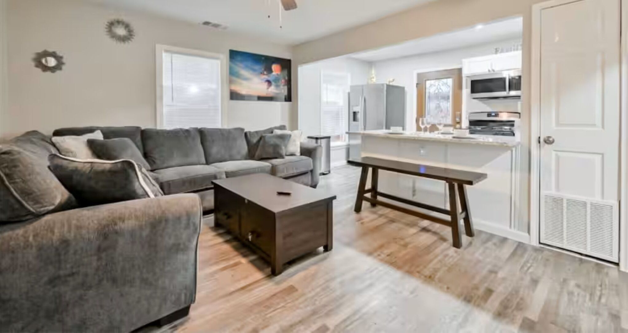 A living room with a grey sofa, a coffee table, and a kitchen area with a fridge and oven.