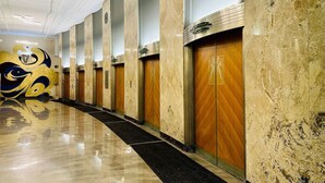 Un couloir d’hôtel aux murs de marbre, aux portes en bois et au sol réfléchissant.