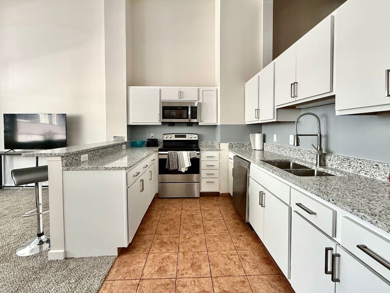 A modern kitchen with white cabinets, a stainless steel oven, a microwave, and a granite countertop.