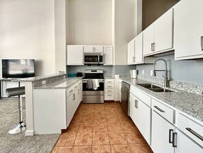Eine moderne Küche mit weißen Schränken, einem Edelstahlbackofen, einer Mikrowelle und einer Arbeitsplatte aus Granit.
