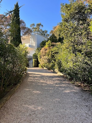 A gravel pathway leading to a building with a white exterior, surrounded by dense shrubbery and trees. - Rayol, 5-bedroom villa with pool, 100 m from the beach (Rayol-Canadel-sur-Mer)
