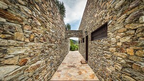 A stone pathway leading to a stone building with a view of greenery in the distance.