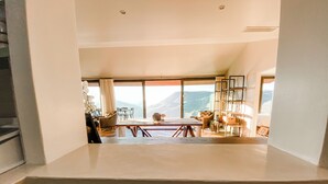 A kitchen with a view of a balcony, a dining area with chairs, and a shelf with glassware.