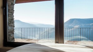 A bedroom with a large window, a bed, and a view of mountains.