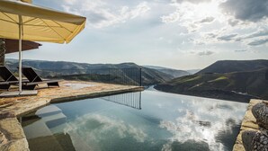 An infinity pool with a view of a valley, outdoor seating, and a stone structure.