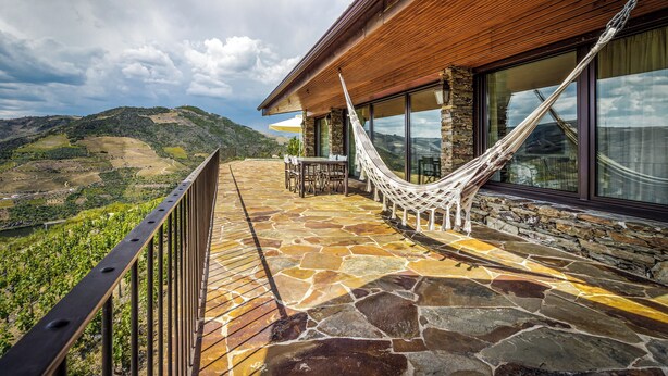 A stone patio with a hammock, wooden railing, and a view of the landscape.