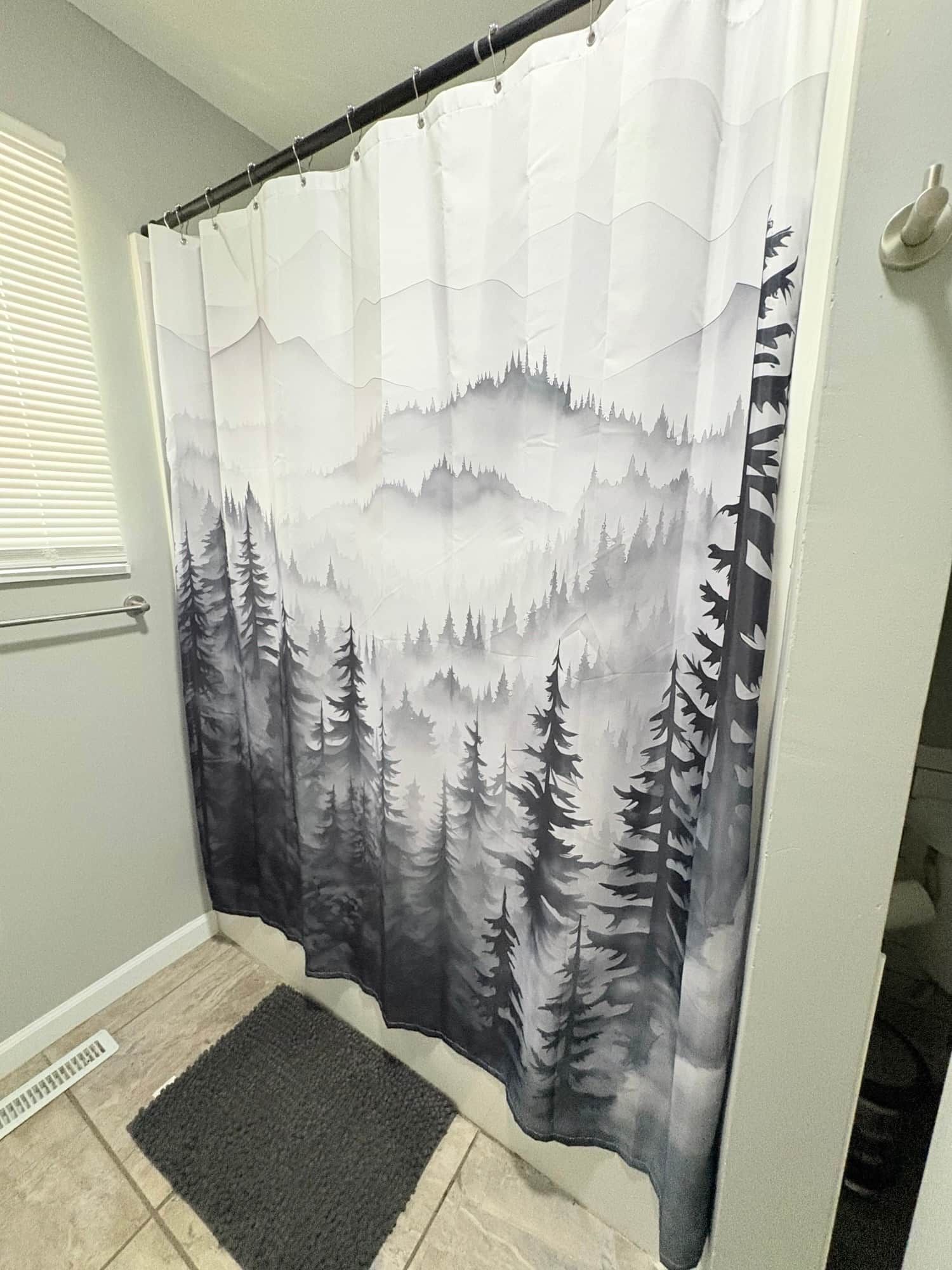 Une salle de bain avec un rideau de douche orné d’un motif représentant une forêt et des montagnes.