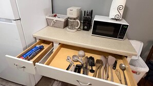 Une cuisine équipée d’un four à micro-ondes, d’une machine à café et de divers ustensiles rangés dans un tiroir.