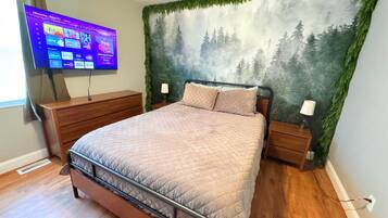 Un dormitorio con cama, cómoda, televisor montado en la pared y un mural con motivos forestales.