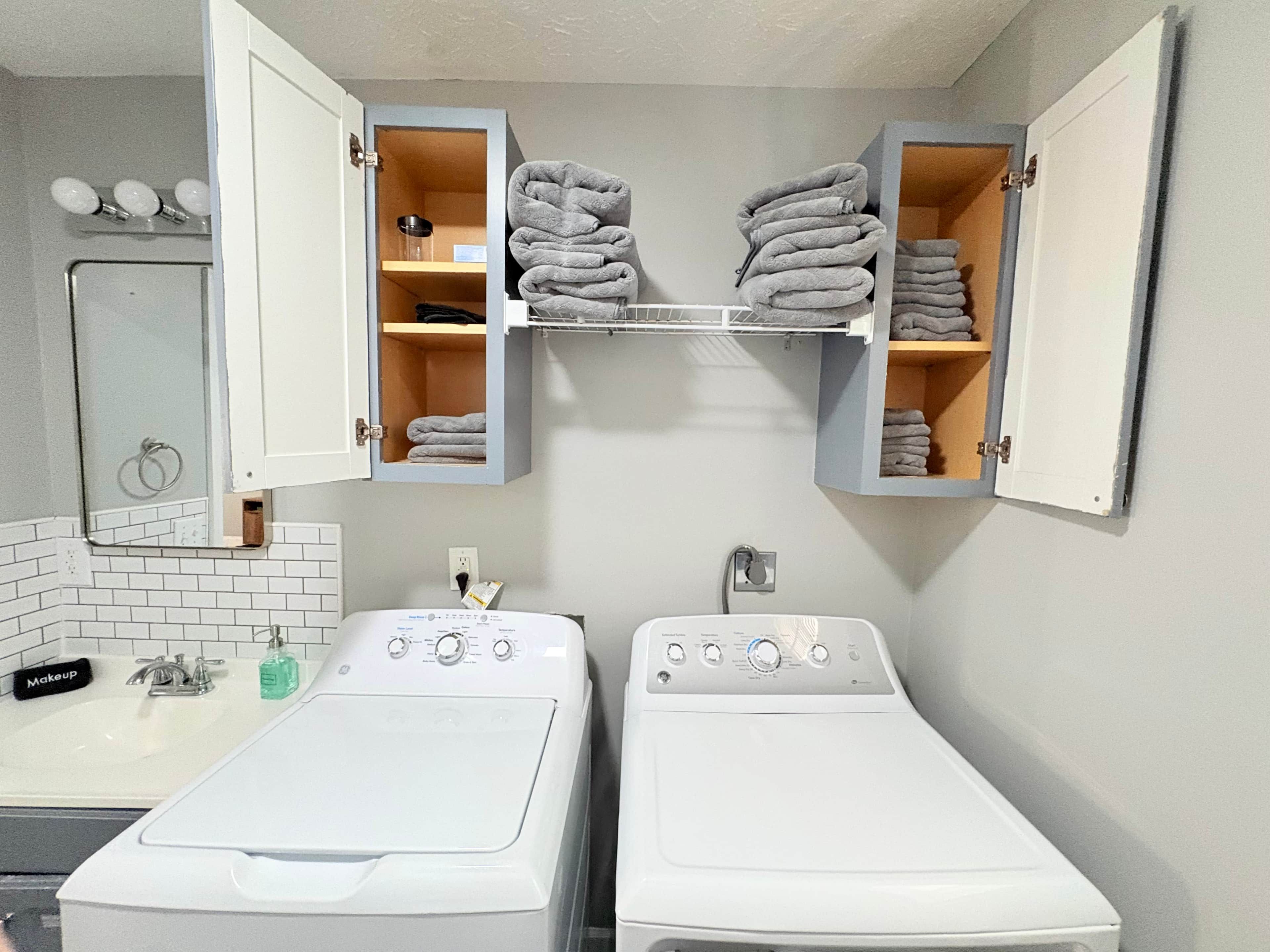 A laundry room with two washing machines, a mirror, and towel storage.
