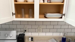 Une cuisine avec des meubles blancs, une cuisinière, un grille-pain et un organiseur de tiroir contenant des ustensiles.