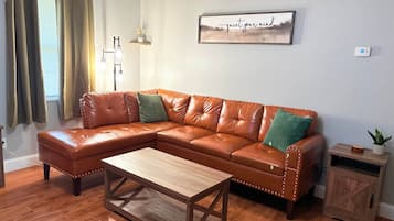 Ein Wohnzimmer mit einem braunen Ledersofa, einem Couchtisch aus Holz, einer Wandleuchte und einem gerahmten Kunstwerk mit der Aufschrift 'quiet your mind'.