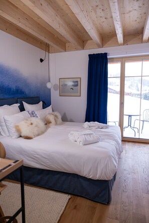 A bedroom with a wooden ceiling, a bed with white bedding, a desk with a chair, and a view of a snowy landscape through a glass door. - La Tzoumaz Lodge, 4 Vallées luxury chalet, daily housekeeping, sleeps 10 to 12 (Riddes)