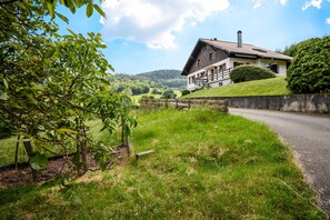 A house with a sloped roof, a chimney, and a stone wall. - Apartment “Au Petit Chamois” with Mountain View, Private Garden and Wi-Fi (Breitenbach-Haut-Rhin)