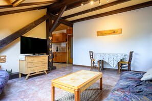 Un salon chaleureux avec une table en bois, un canapé, un téléviseur et, au fond, une cuisine.