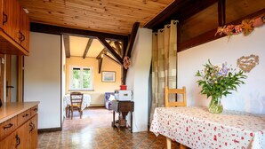 A room with a wooden ceiling, a dining table with a white tablecloth, a vase with flowers, and a wooden cabinet.